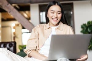 Happy asian woman resting at home with laptop, watching videos or browsing website on computer