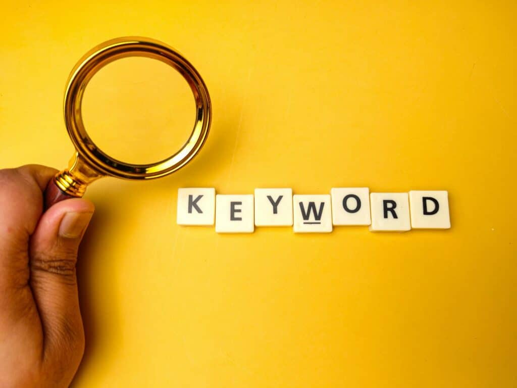 Hand holding a magnifying glass against ayellow background with the word KEYWORD.